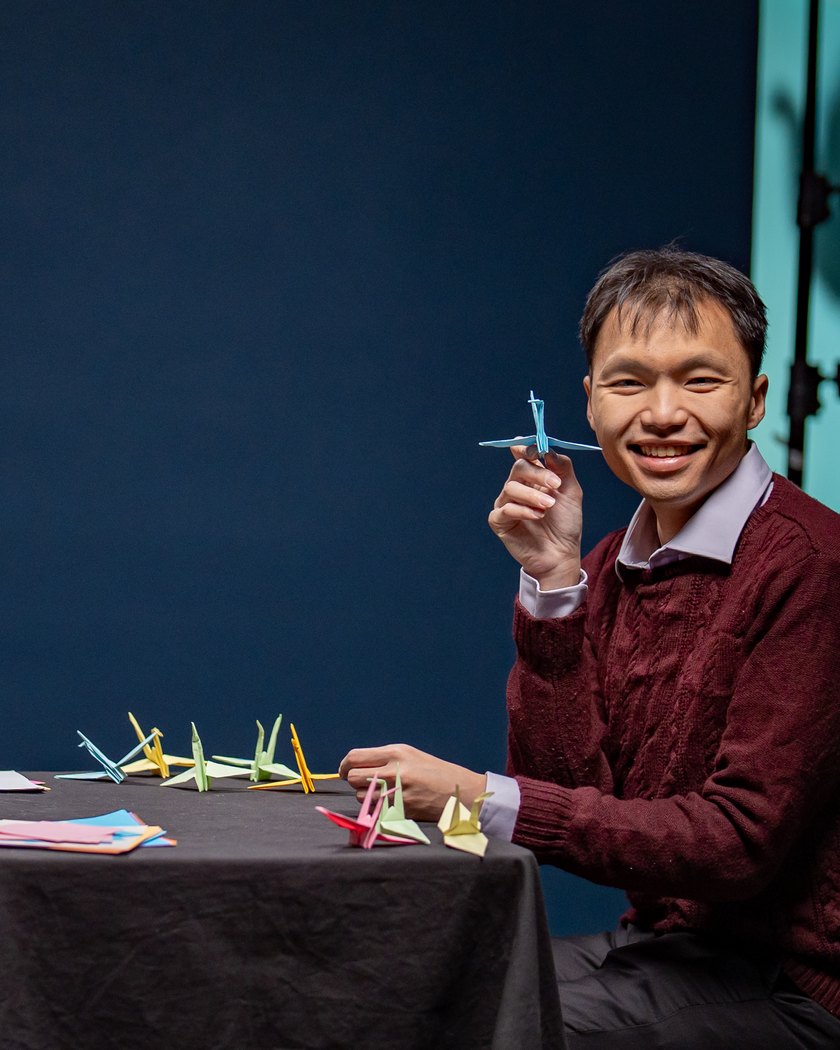 Dr Eric Hadinata smiling and holding a paper crane at a table